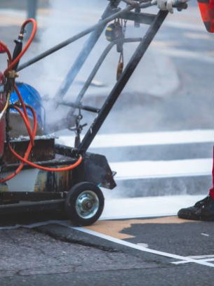 Process of making new road surface markings with a line striping machine, workers improve city infrastructure, demarcation marking of pedestrian crossing with a hot melted paint on asphalt pavement